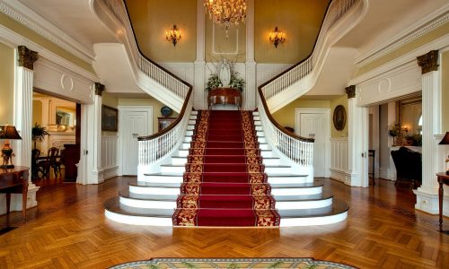 Grand staircase with red carpet in a luxurious hotel lobby, highlighted by a chandelier.